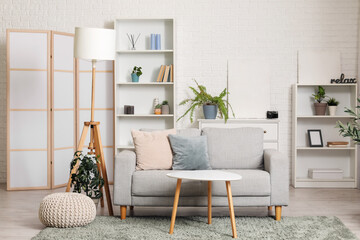 Interior of stylish living room with folding screen, grey sofa, shelving unit and coffee table