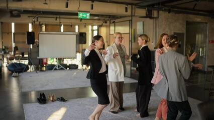 A group of confident girls in business suits dance during a break at work on a gray carpet during a happy time at work in a modern office