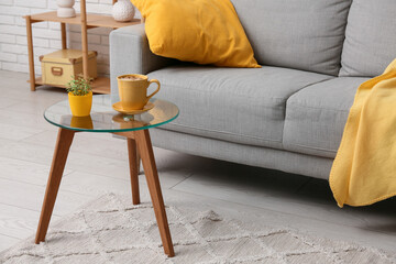 Interior of stylish living room with grey sofa, cup on coffee table and pillow, closeup