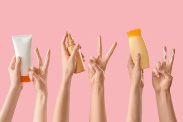 Female hands with sunscreen cream showing Victory gesture on pink background
