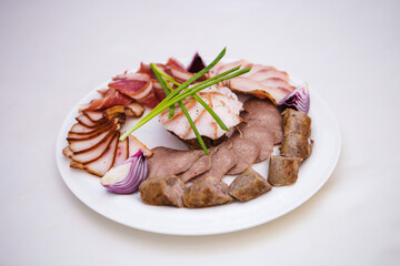 A plate of assorted meats and vegetables, including onions and celery, is arranged on a white table