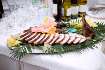 A large fish is displayed on a table with a variety of other food items and drinks. The table is set with many wine glasses and cups, and there are also some forks and knives