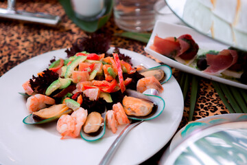 A plate of food with shrimp, avocado, and other vegetables. The plate is set on a table with other plates and utensils