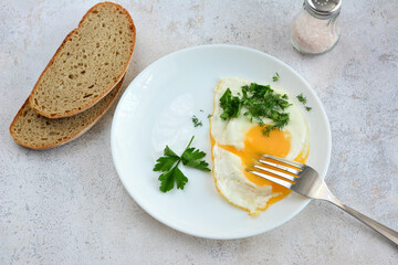 a plate with fried egg and parsley on a table with slices of bread    