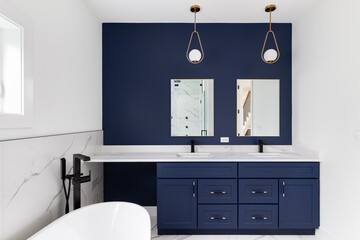 A luxury bathroom with a blue cabinet and accent wall, gold lights hanging above the marble...