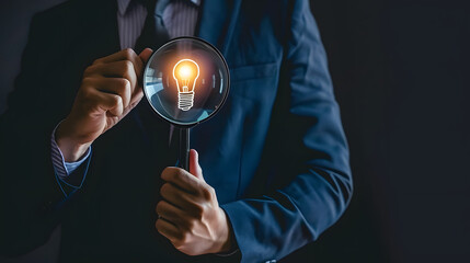 Businessman holding a magnifying glass with a light bulb icon on a black background 