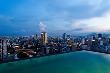 Evening view of Da Nang, Vietnam, with high-rise buildings reflecting in a rooftop pool. The sky is...