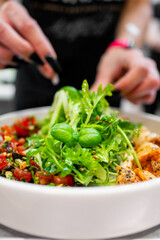 Close-up of a hand garnishing a dish with herbs, featuring grilled shrimp and fresh salad.