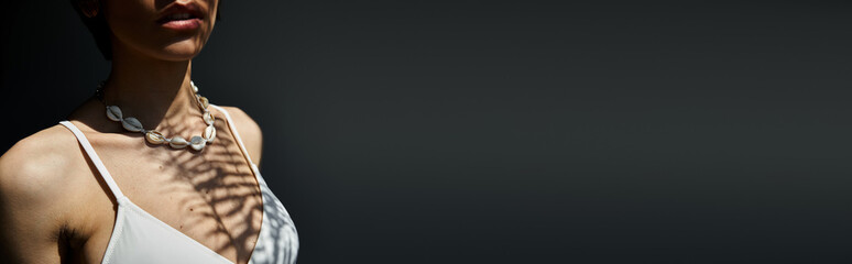 A stylish young woman in a white top gracefully poses with a necklace.