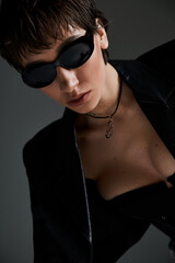 A beautiful young woman poses confidently in black sunglasses for a fashion shoot.