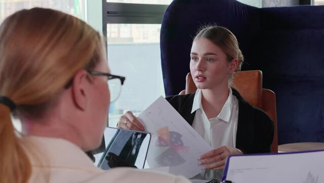 Confident blonde businesswoman girl in business clothes distributes to her colleagues the necessary schedules for an interview and a general meeting to solve a problem in a modern office