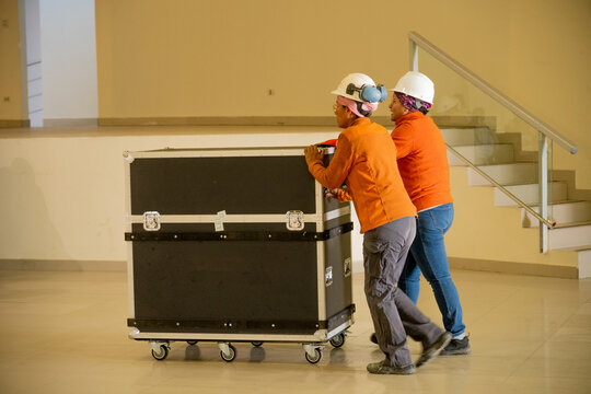 Two workers pushing a flightcase to set up a stage in an auditorium
