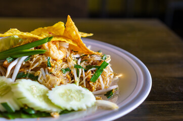 fried noodle thai style with prawns, pad thai with prawns bean sprout and garnish peanuts sugar lemon lime chili powder on plate on wooden table.