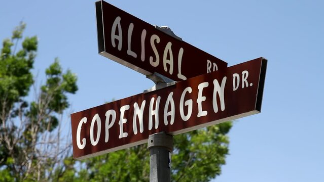 Copenhagen Drive road sign in Solvang, California. Set against a clear blue sky, the sign stands prominently while blurred trees in the background sway gently in the wind.