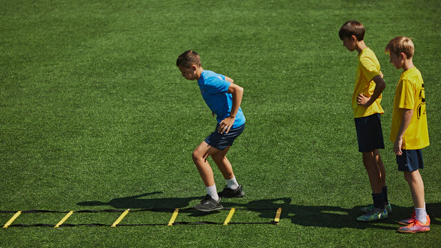 Youth Soccer Training. Young soccer players, boys practice footwork on agility ladder during focused training session. Outdoor field. Concept of sport, school, childhood, hobby, active lifestyle