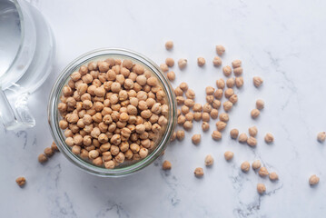 Dried chickpea in a glass bowl on white marble background.