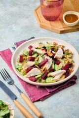 Healthy salad with boiled beets, chicken breast, iceberg lettuce, walnuts and peanut dressing on a ceramic plate on a gray concrete background. Salad recipes.