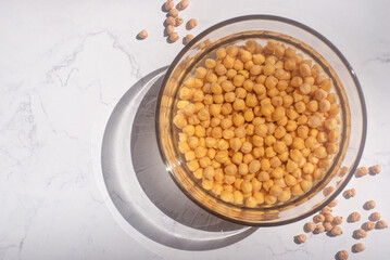 chickpea soaked in water in a glass bowl on marble table.