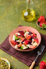 Healthy salad of boiled beets, mozzarella and fresh strawberries, dressed with olive oil and sprinkled with pumpkin seeds, in a pink ceramic plate on a green concrete background.