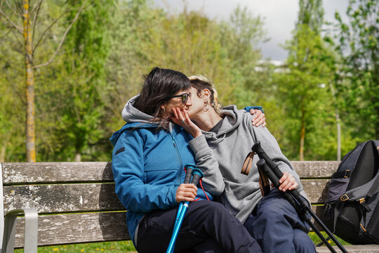 Non binary friends kissing sitting in a public park.