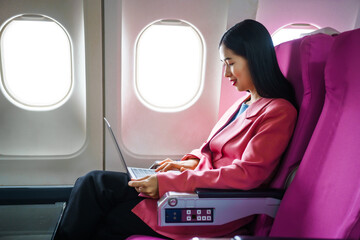 A young Asian female airplane passenger sits by the window during the flight, holding her boarding...
