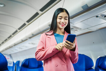 A young Asian female airplane passenger sits by the window during the flight, holding her boarding...
