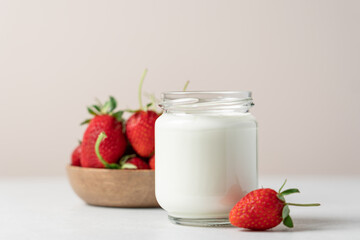 Natural yogurt in a glass jar and strawberries on a light background with copy space