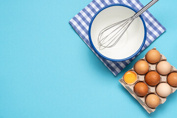 Eggs, bowl and whisk on blue background with copy space. Baking background top view