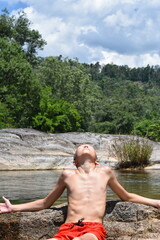 A day on the river, a boy in shorts throws back his head and sunbathes in the sun.