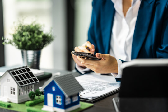 A businesswoman is reviewing contract papers at her desk in a sustainable house and condo, emphasizing clean energy with a nearby wind turbine powering the neighborhood.