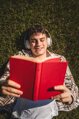 Young boy with headphones lying down on the grass and read a book