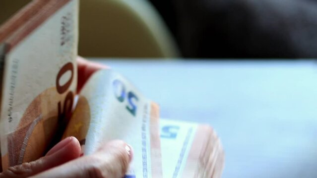 Close-up of female hands counting a stack of  euros, flipping through monry banknotes methodically. Detailed view of woman's hands as she counts and examines a bundle of cash euro bills