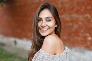 Beautiful young fresh woman with a cute smile wearing a knitted sweater on a red brick background