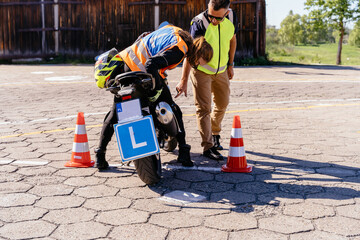 Fototapeta premium Motorcycle driving practice. Learner motorcyclist practicing to ride a moto. Learner biker on test road with red cones. Instructor writing on clipboard his points.