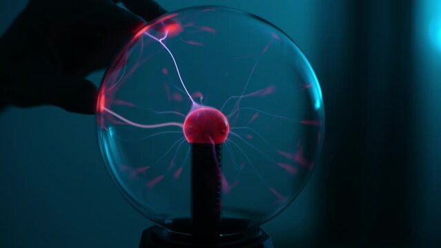 Close-up palm of unrecognizable man touching electric plasma ball with luminous flames during physical experiment. Closeup of plasma ball with many energy rays inside. Shooting in slow motion.