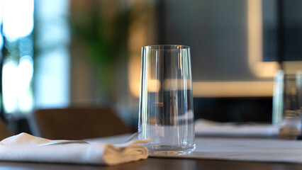 A transparent glass stands on a table against the backdrop of a restaurant. Cloth napkins. Elegant style
