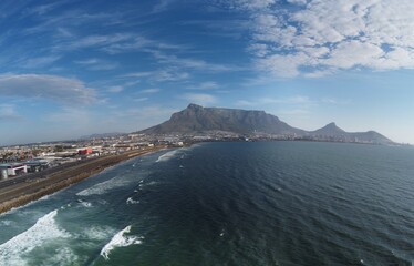 Panoramic photo of coastline close to Cape Town showing Table Mountain and industrial area with railway track.