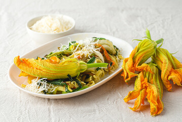 Tagliatelle pasta with zucchini flowers (fiori di zucca), green onions. Italian spring, summer pasta recipes, healthy cooking. Recipes with flowers, natural eco style
