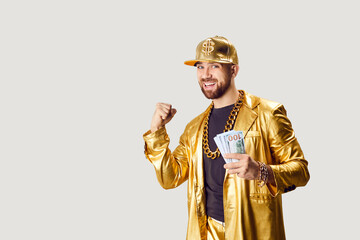 Happy excited funny man in golden suit holding money dollars cash banknotes in hands making yes...