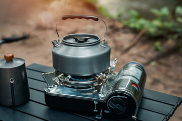 Camping, teapot on gas stove on wooden table in nature, coffee equipment set on the table