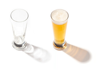 Glass and a full glass of light beer with foam, placed side by side on a white background. The contrast between the empty and full glasses, along with the shadows and reflections