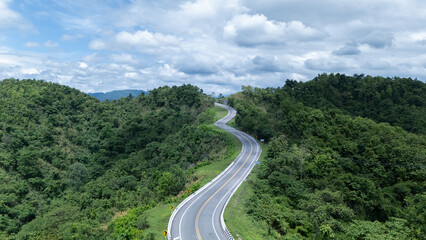 Aerial view from above of country road through the green summer forest in summer Thailand. Top view of the asphalt road and dense green forests.