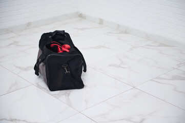 Black duffel bag with gym equipment on white marble floor in minimalistic room