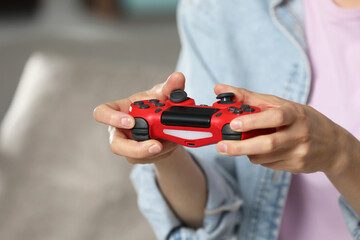 Woman playing video game with controller at home, closeup. Space for text