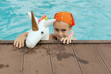 Closeup portrait of little girl with inflatable unicorn for swimming. Happy child having fun in water, beach resort, summer vacation and holidays concept. Girl showcasing a joyful summer vibe.