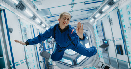 Portrait of a Courageous Caucasian Female Astronaut on Board a Spacecraft, Floating in Zero Gravity and Smiling At The Camera, Waving. Space Travel, Solar System Exploration and Colonization Concept