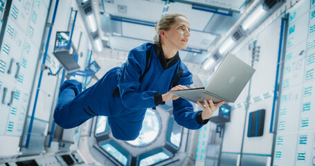 Female Astronaut Using Laptop Computer in Space Inside a Spacecraft. Working Online, Checking and...