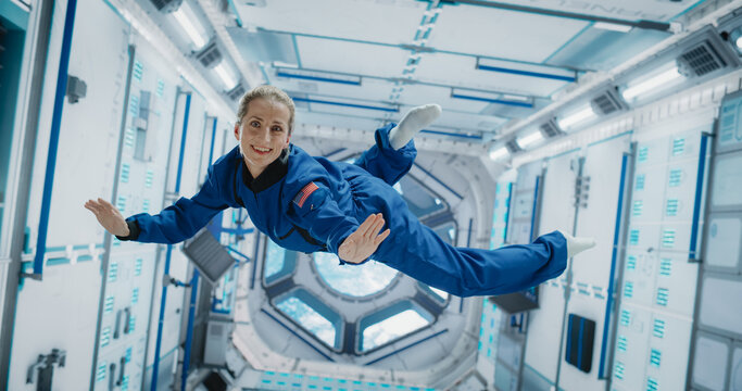 Portrait of a Courageous Caucasian Female Astronaut on Board a Spacecraft, Floating in Zero Gravity and Smiling At The Camera, Waving. Space Travel, Solar System Exploration and Colonization Concept