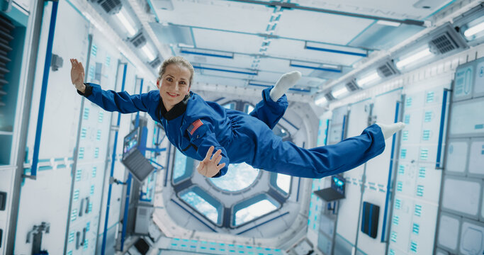 Portrait of a Courageous Caucasian Female Astronaut on Board a Spacecraft, Floating in Zero Gravity and Smiling At The Camera, Waving. Space Travel, Solar System Exploration and Colonization. - Powered by Adobe
