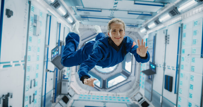 Portrait of a Courageous Caucasian Female Astronaut on Board a Spacecraft, Floating in Zero Gravity and Smiling At The Camera, Waving. Deep Space Travel, Solar System Exploration and Colonization. - Powered by Adobe